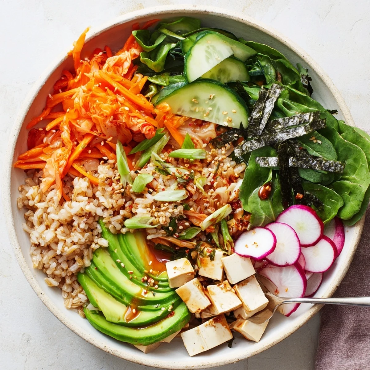 A colorful fermented vegetable bowl with kimchi, fresh greens, and avocado slices.  