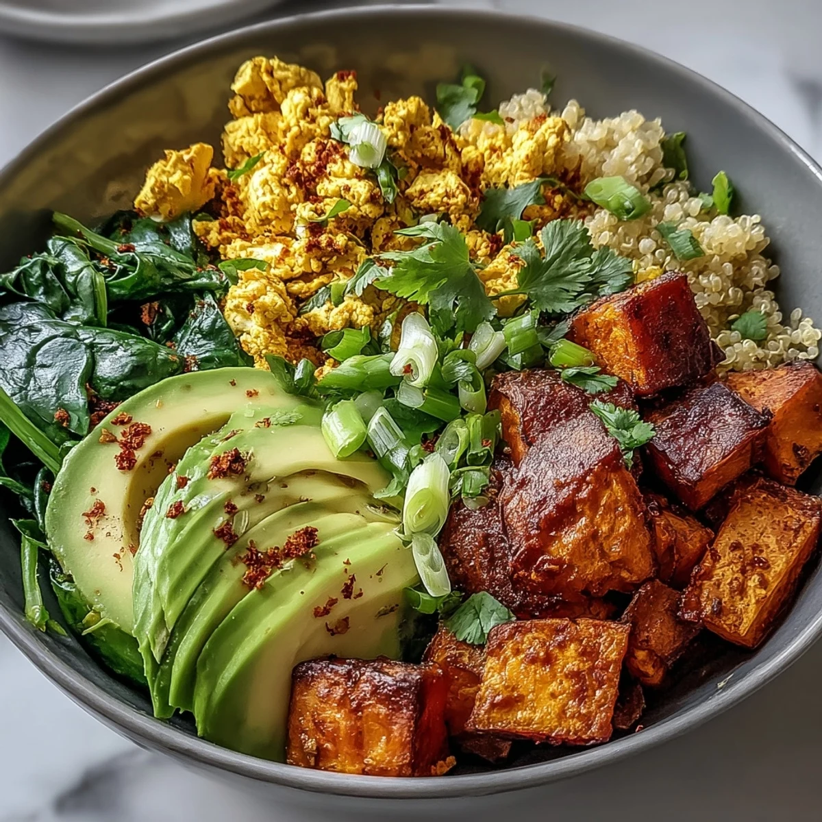 Close-up of a vibrant Tofu Scramble Vegan Breakfast Bowl featuring golden tofu, roasted sweet potatoes, and creamy avocado slices.