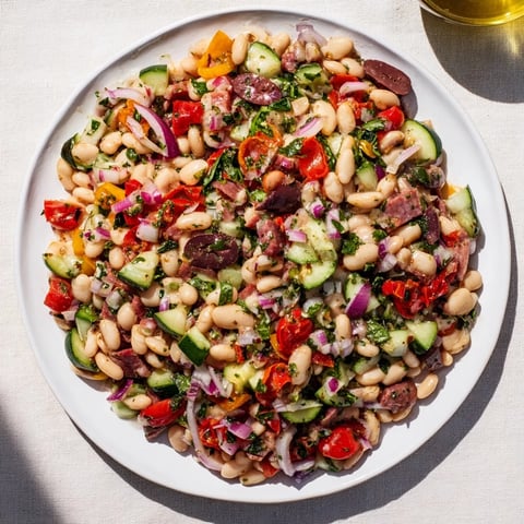 Mediterranean Dense Bean Salad showcases a colorful array of beans, salami, and vegetables, ready to serve.