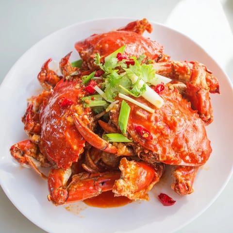 Steaming Singaporean Chili Crab, covered in a rich red sauce, garnished with green onions.