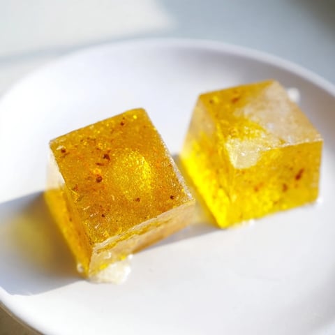 Golden Lemon Ginger Turmeric Wellness Cubes sit in a clear ice cube tray, their vibrant orange hue promising a zesty, immune-boosting chill.