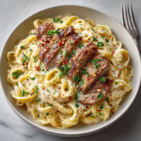 Juicy steak served atop creamy pasta, parmesan cheese melting into the rich sauce.