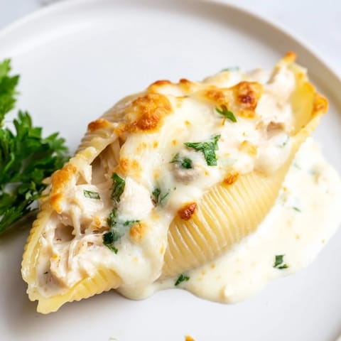Golden-baked Chicken Alfredo Stuffed Shells bubbling with creamy cheese sauce and tender pasta in a white dish.