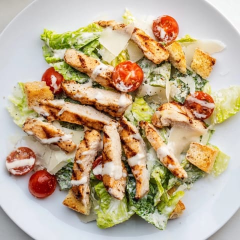 A vibrant bowl of Yogurt Caesar Grilled Chicken Salad with juicy grilled chicken, fresh cherry tomatoes, and shaved Parmesan cheese.
