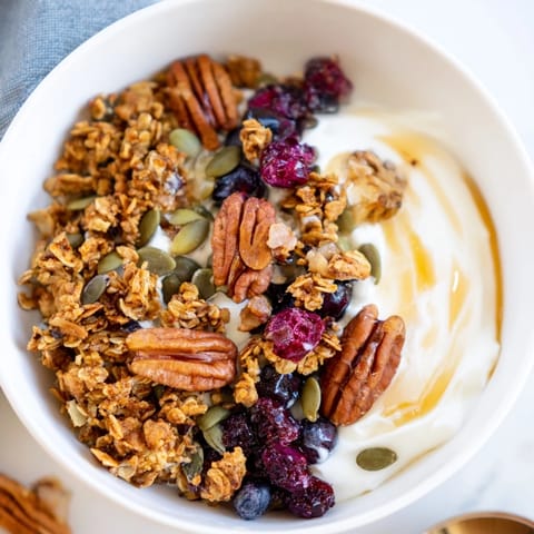 The Yogurt Bowl with Winter Berries and Spiced Crunch is garnished with pomegranate seeds, walnuts, and a drizzle of maple syrup.