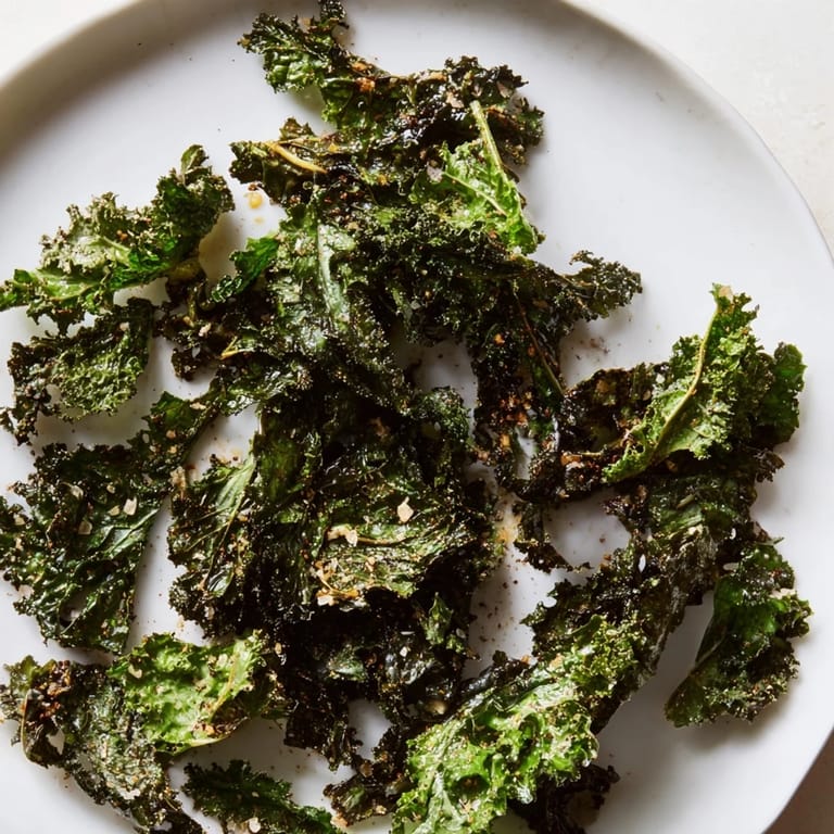 Homemade baked kale chips, perfectly crisp, served as a vegan, gluten-free snack alongside a crisp drink.