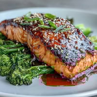 A glistening honey soy glazed salmon fillet rests on a bed of crisp sesame broccoli, garnished with fresh scallions and lime.  