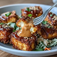 Crispy baked tofu cubes with brown rice and colorful vegetables, drizzled in rich peanut sauce for a satisfying vegan bowl.  